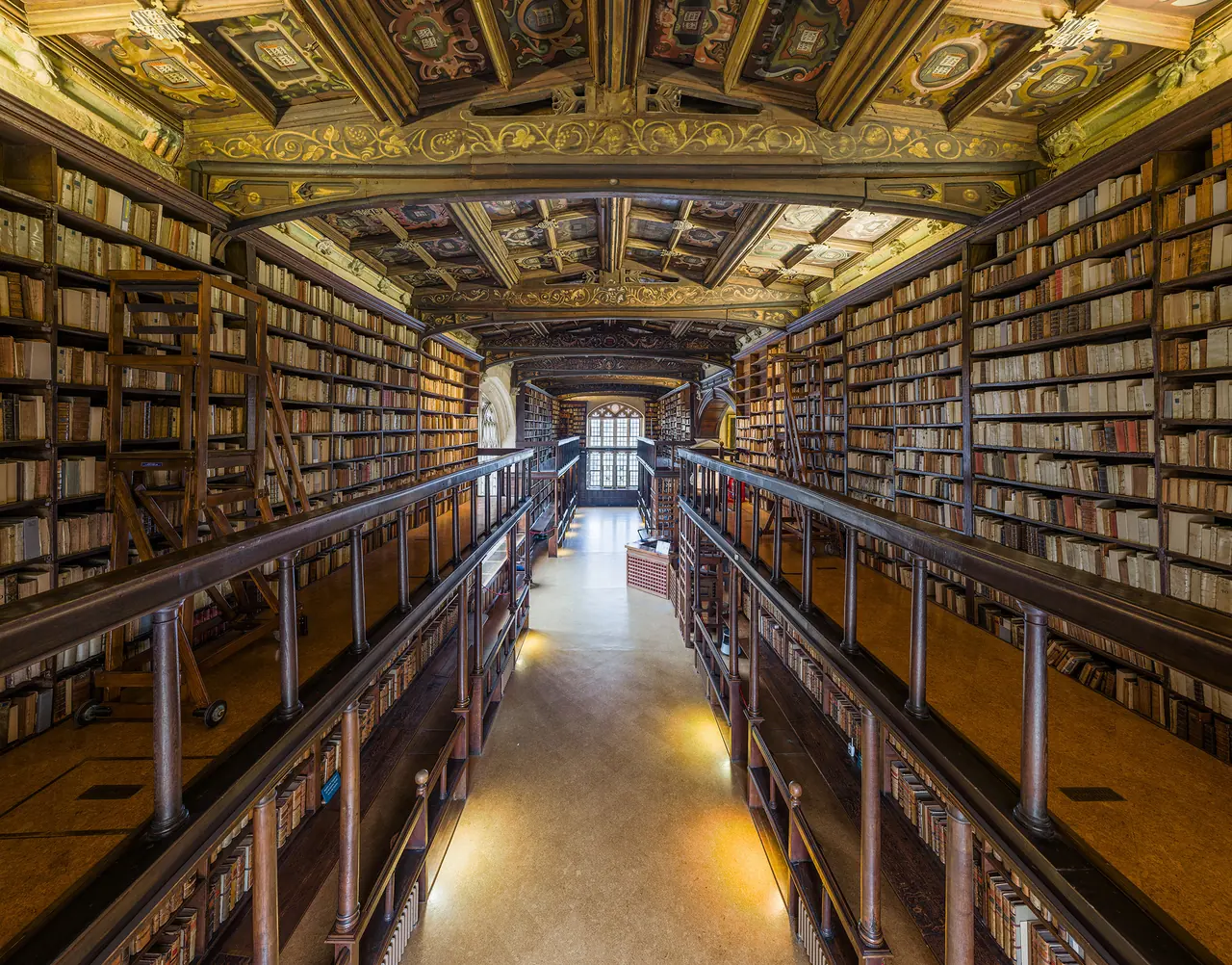 A long aisle of Duke Humfrey's Library, shelves of old books on both sides beneath a painted ceiling