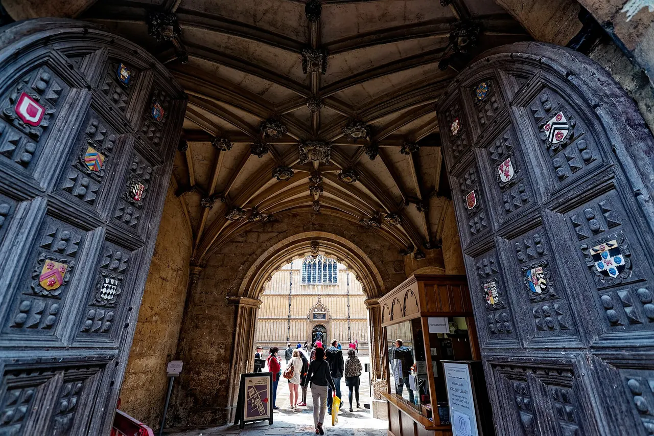 Looking through an archway into the Old Schools Quadrangle towards the Proscholium doors and a bronze statue